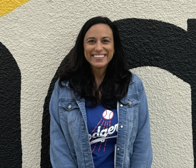 The new VP, Andrea Medrano, stands in front of the murals near a building. 