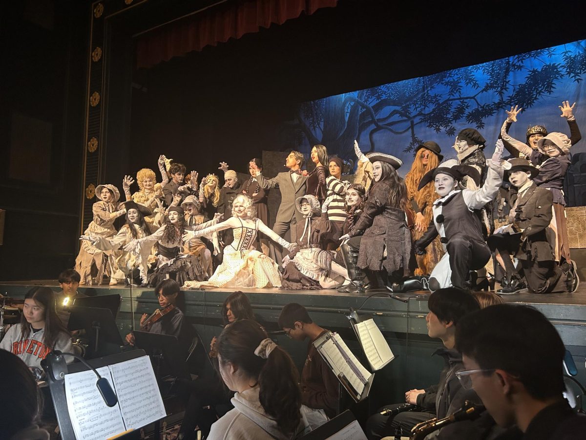 The titular Addams family poses on stage with their ancestors.